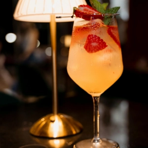 VerGin Bloom Berry Fizz VerGin SA Mocktail with strawberries and mint in a wine glass with a lamp and warm aesthetic background.