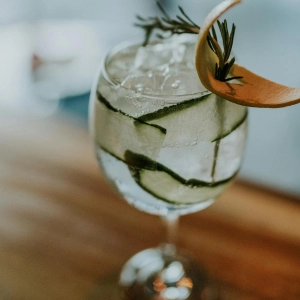 VerGin Limón Cucumber Cooler VerGin Limón Mocktail with cucumber ribbons and a spring of rosemary in a big cocktail glass on a wooden table.